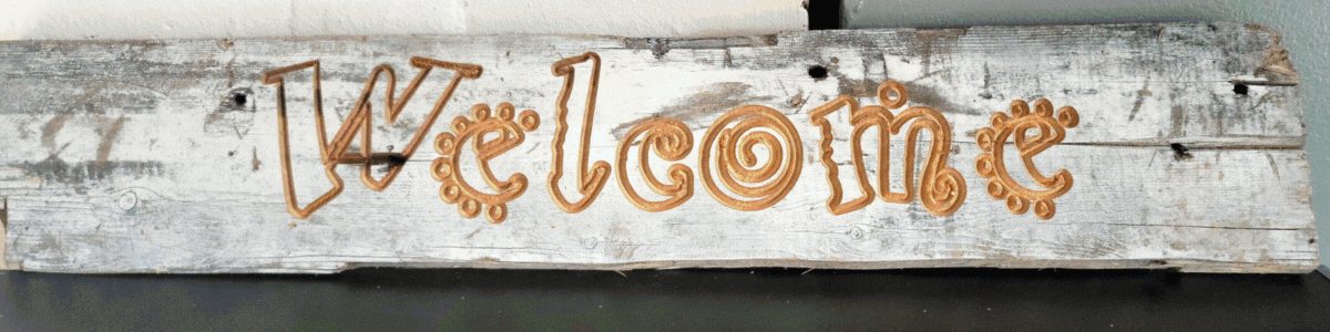 A weathered board with the word Welcome carved into it in flowing letters.